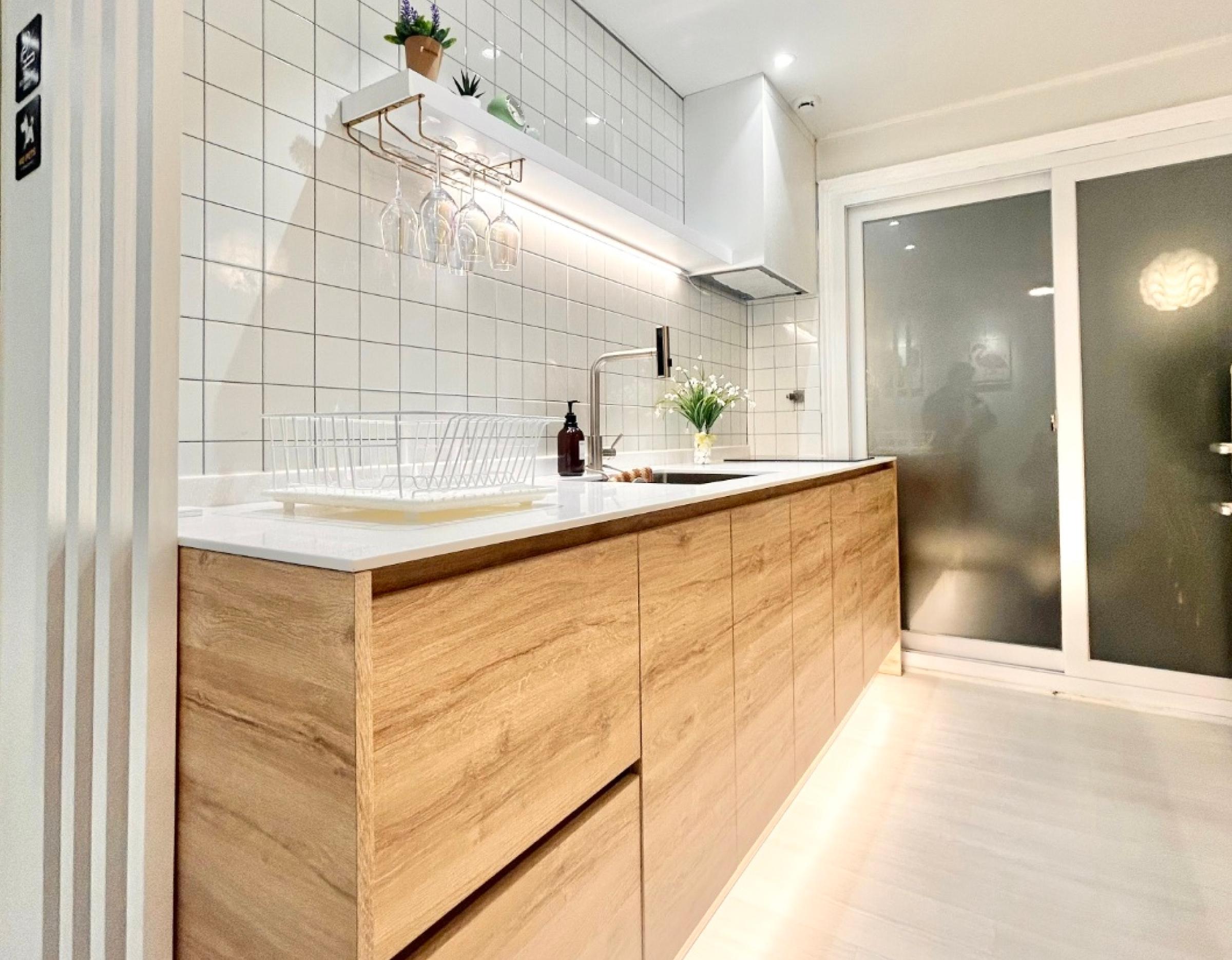 Minimal modern kitchen with wood lower cabinets, white countertop, tiled backsplash, hanging wine glasses and sliding frosted door