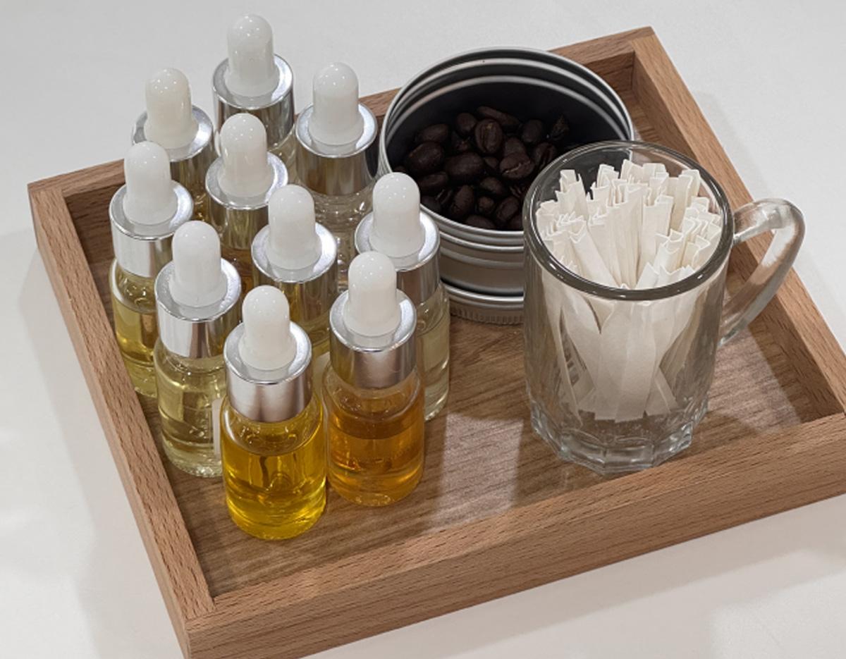 wooden tray with small dropper bottles of golden perfume oil, tin of coffee beans and glass mug holding folded scent strips