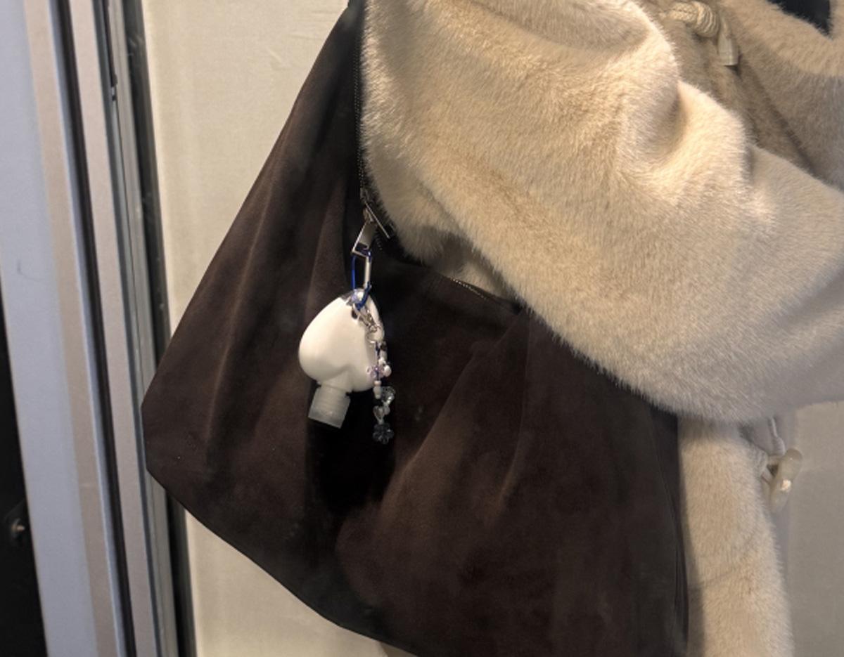 brown suede shoulder bag with a white heart-shaped hand cream bottle keyring and beaded charm hanging from strap