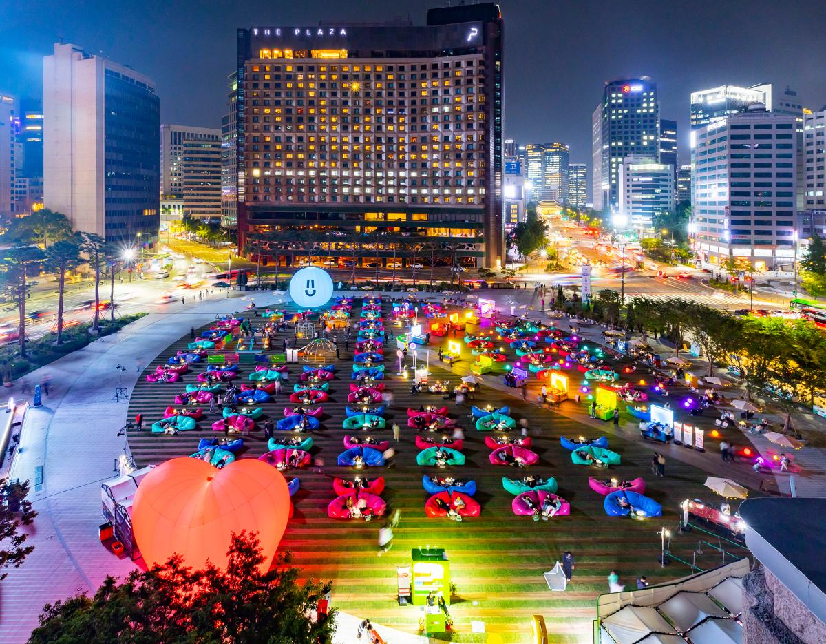 nighttime Seoul Plaza lawn filled with colorful beanbags, glowing heart lantern and visitors reading during outdoor library event