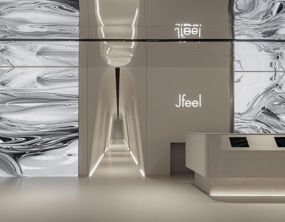Minimalist clinic lobby with illuminated Jfeel sign, curved lit corridor and concrete reception desk, marble-pattern wall panels