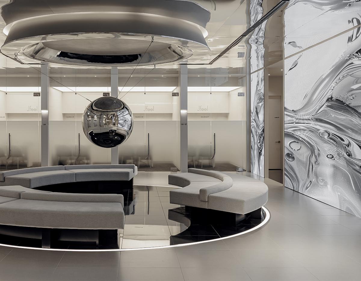 Minimalist clinic waiting area with circular gray modular benches around a reflective black floor and suspended chrome sphere centerpiece