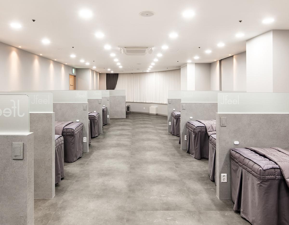 Minimalist clinic treatment room with two rows of partitioned gray treatment beds, soft overhead lighting and tiled floor