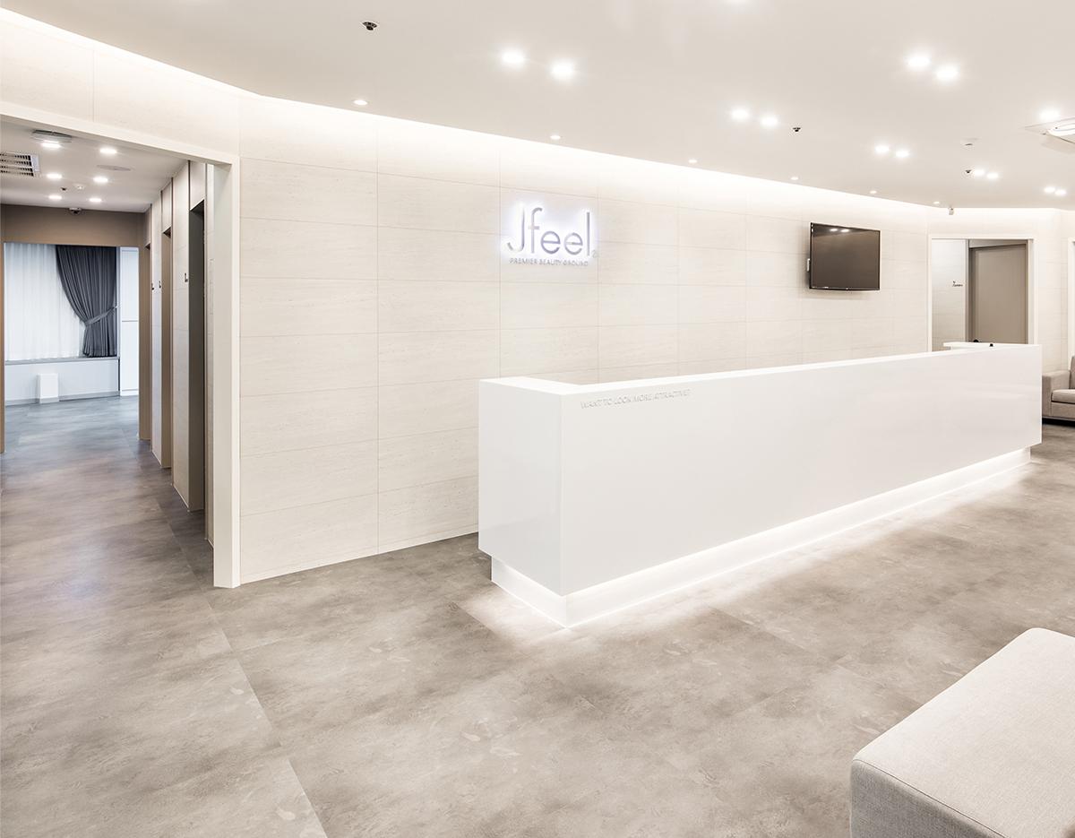 제이필의원 강남점 밝고 미니멀한 흰색 리셉션 데스크와 회색 바닥, 대기 소파가 보이는 클리닉 로비