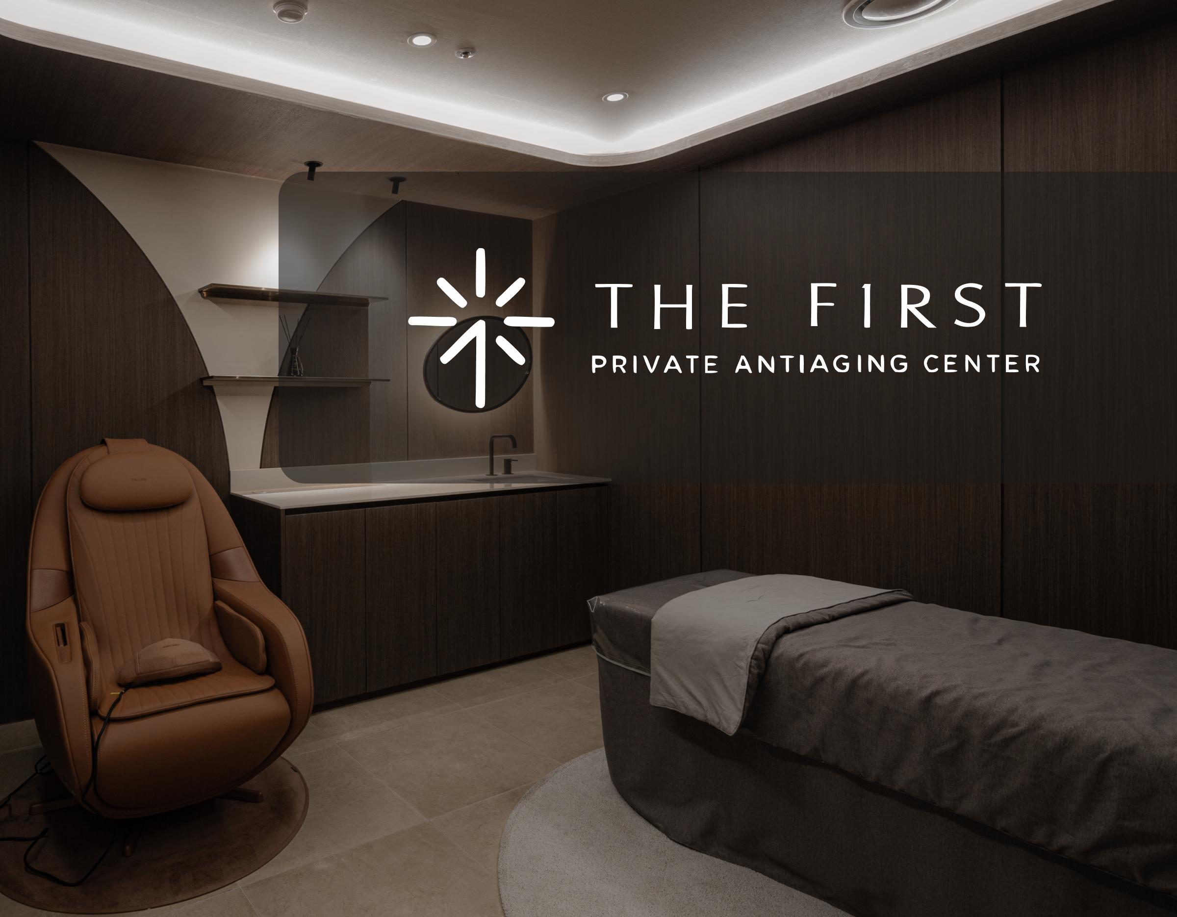 dimly lit private treatment room with brown leather reclining chair, treatment bed and dark wood cabinetry, The First logo visible