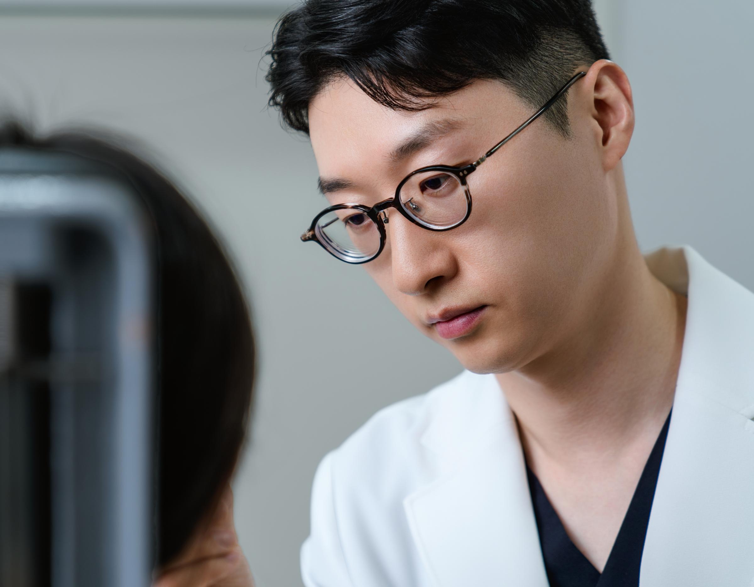 male clinician in white coat speaking to a patient, cropped view showing neck, ear and shoulder with blurred face