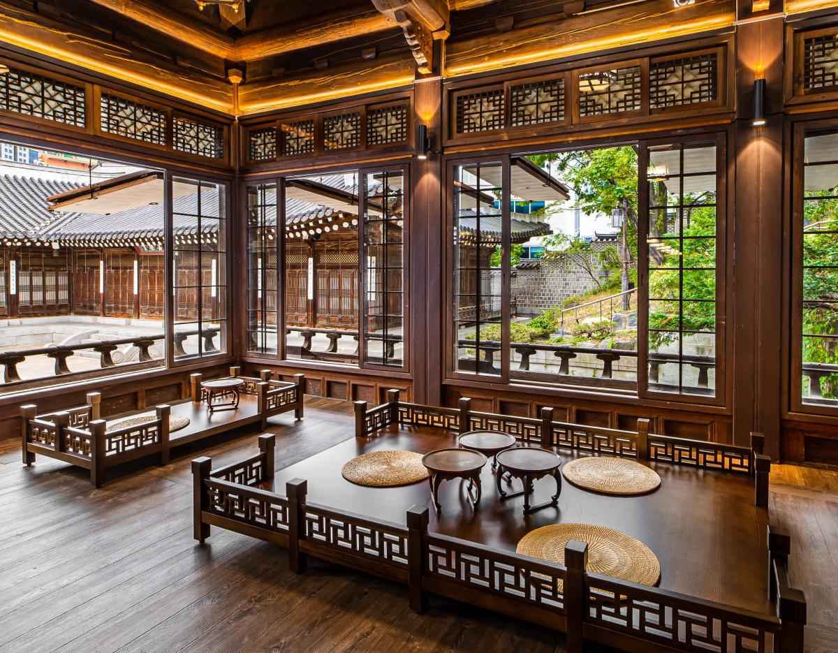 Traditional Korean hanok interior with low wooden tables, round straw seat mats and lattice windows overlooking a courtyard