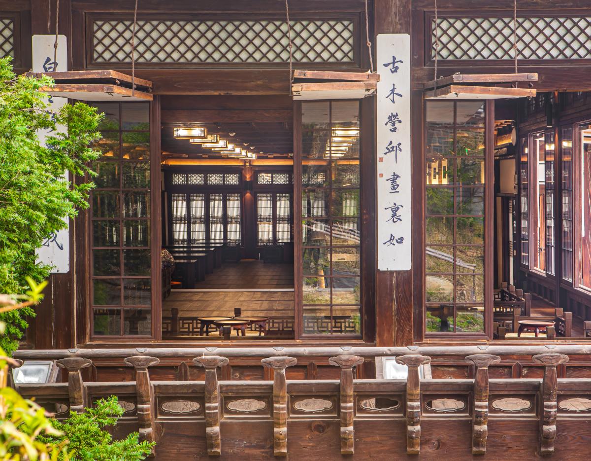 Traditional wooden hanok interior with lattice windows, hanging calligraphy panels, low tables and orchard greenery visible outside