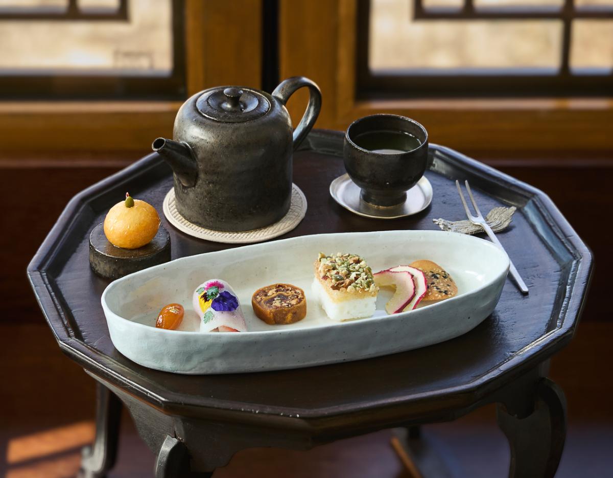 octagonal wooden table with ceramic teapot, cup, and oval plate of assorted traditional Korean sweets and decorative edible flowers