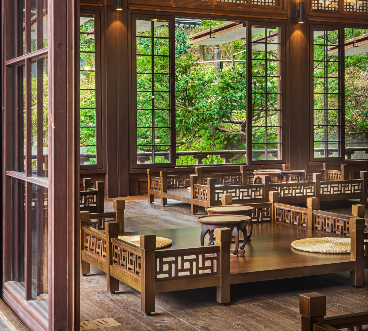 traditional wooden hanok tea room with low latticed tables, straw floor cushions, and large windows overlooking green garden