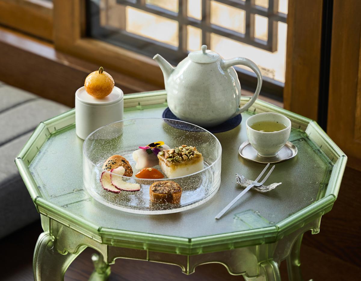 octagonal green lacquered table set with ceramic teapot, teacup, and a clear platter of assorted traditional Korean sweets