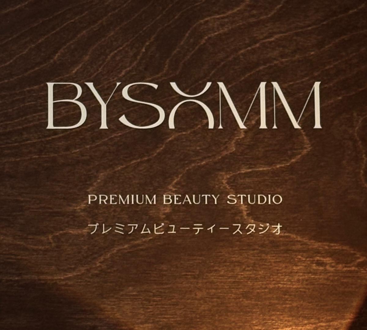 BYSOMM logo in serif type over textured dark wood background with text "Premium Beauty Studio" and Japanese subtitle