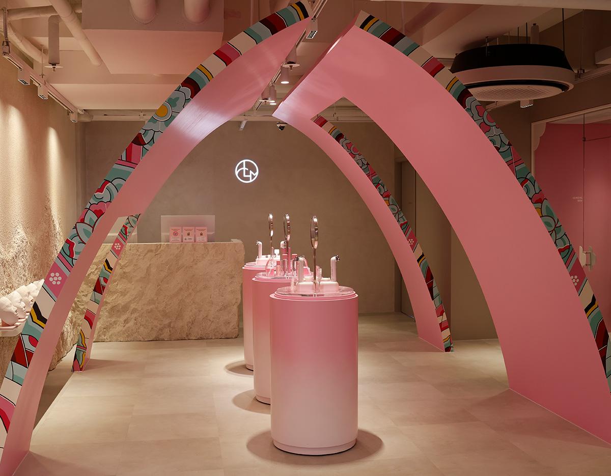 Bright pink salon interior with curved decorative arches, three cylindrical wash stations with mirrors and a stone reception desk