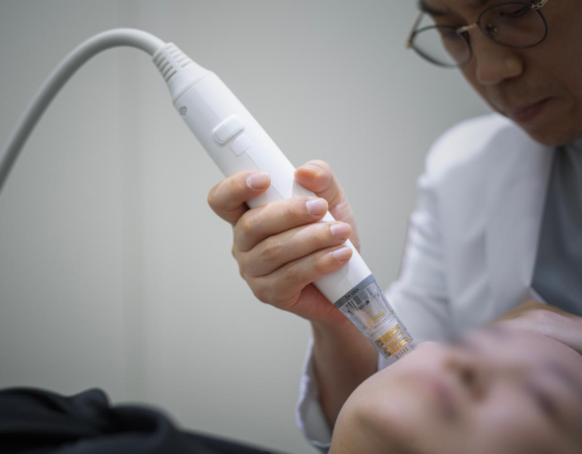 Doctor holding a white microneedling device near a patient's chin during a facial treatment at the clinic.