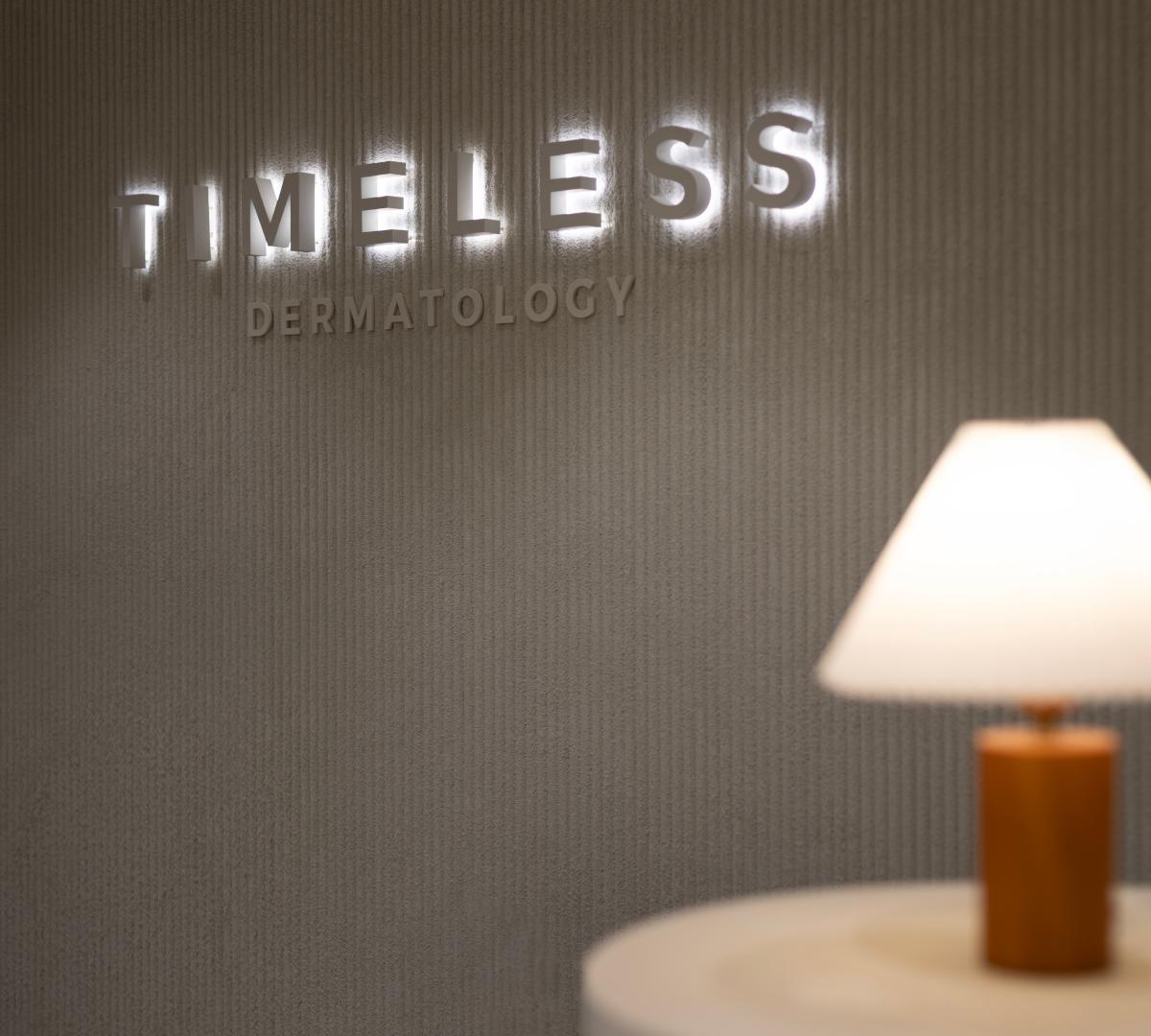 Timeless Dermatology illuminated wall sign with textured background and a blurred table lamp in the foreground