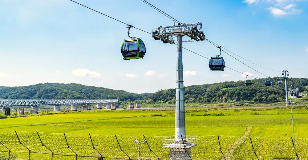 Imjinak cable car crystal gondolas with transparent floors gliding over green rice fields toward distant forested hills