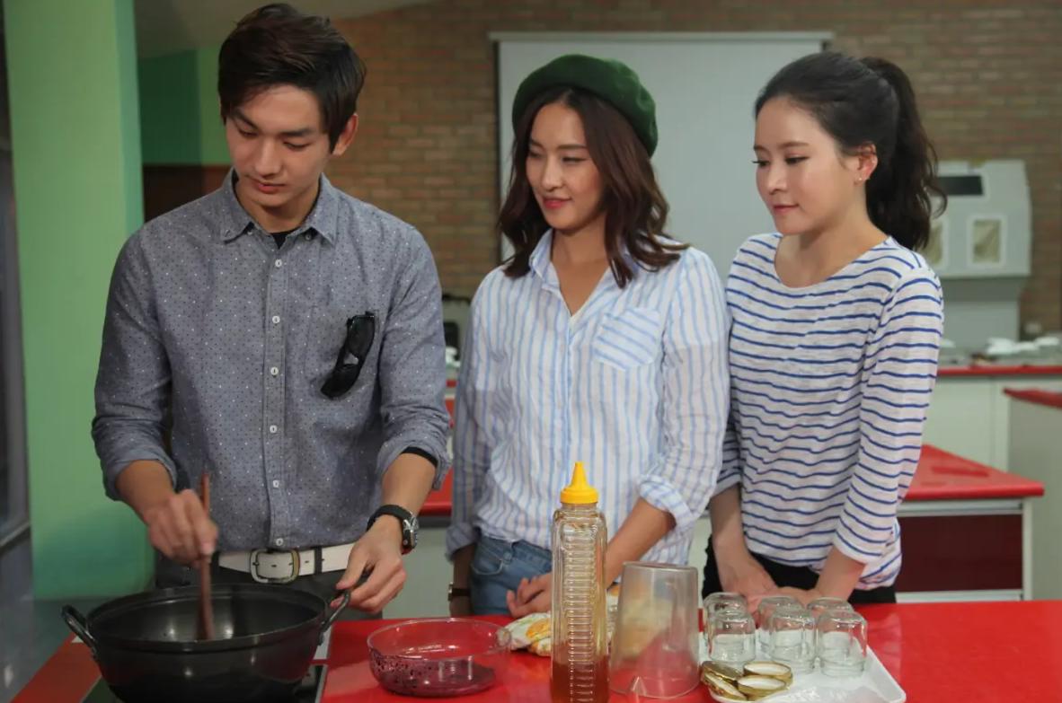 three people standing behind a kitchen counter making jam, utensils, jars and squeeze bottle on red countertop