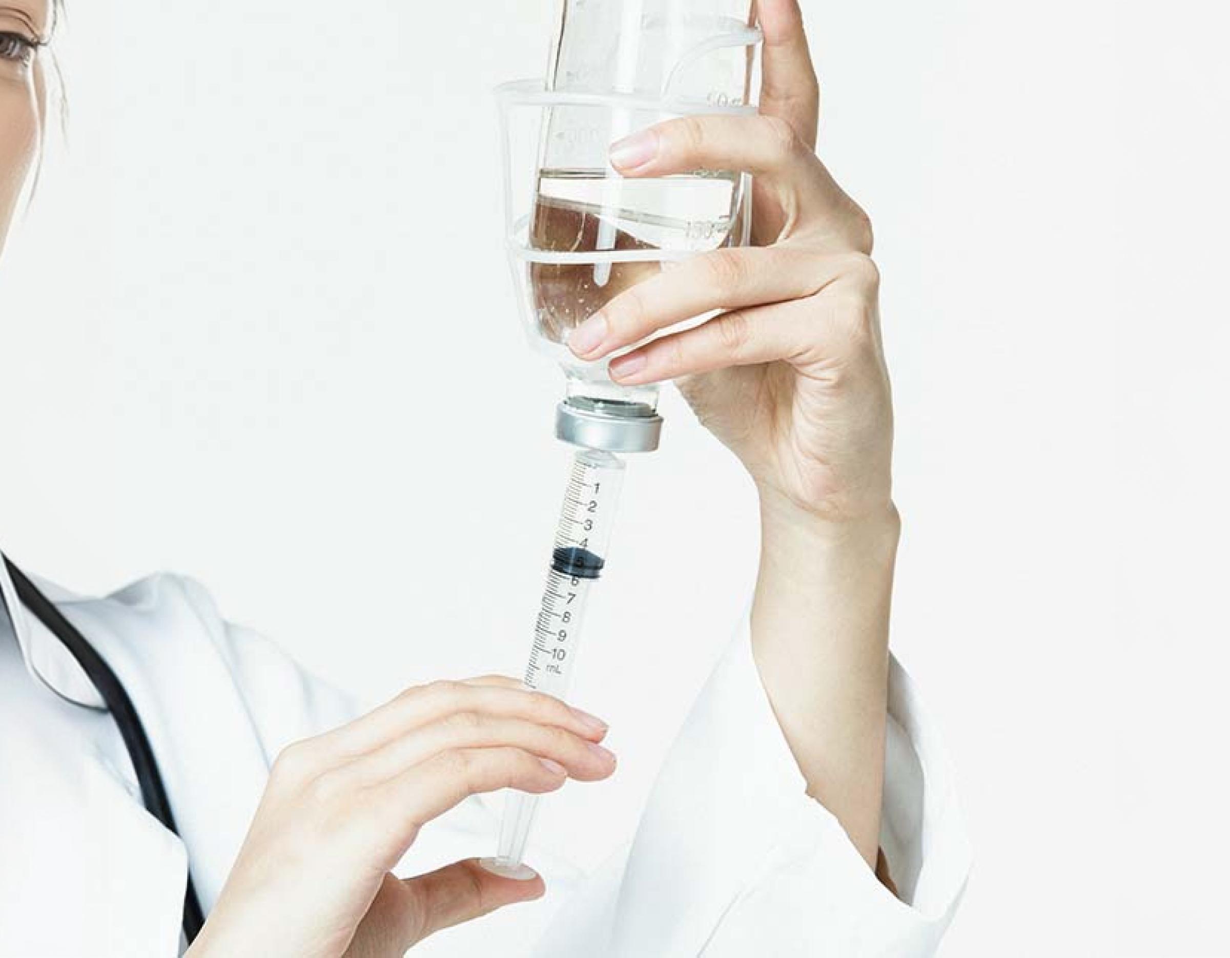 의료진이 IV 수액 병에서 주사기(시린지)로 수액을 채우는 손 클로즈업, 흰 배경