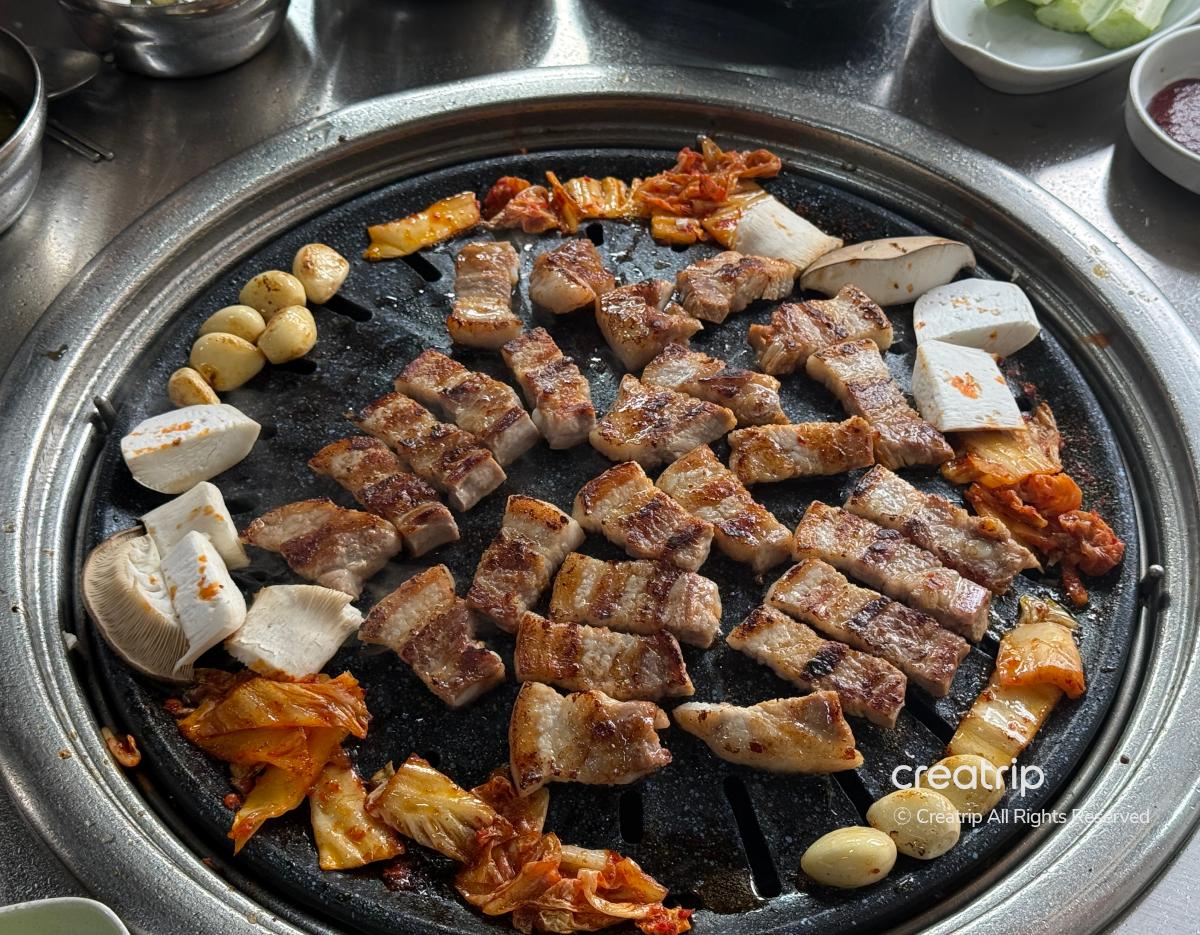 Charcoal grill at Cheonggiwa Galbi with bite-sized pork belly, kimchi, garlic cloves and king oyster mushrooms grilling on cast iron.