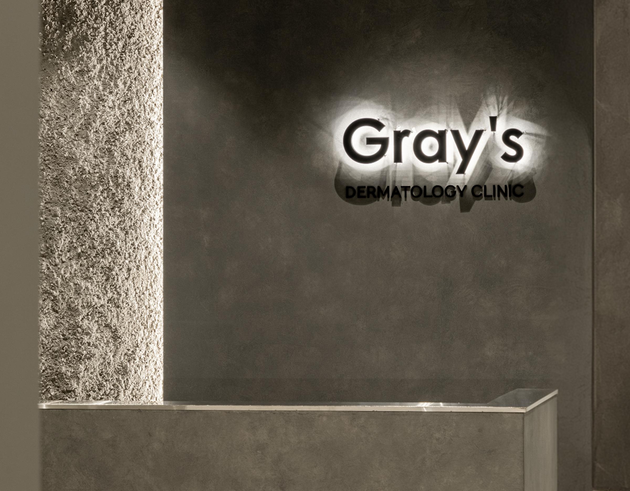 Gray's Dermatology Clinic reception wall with illuminated clinic logo and minimalist concrete counter