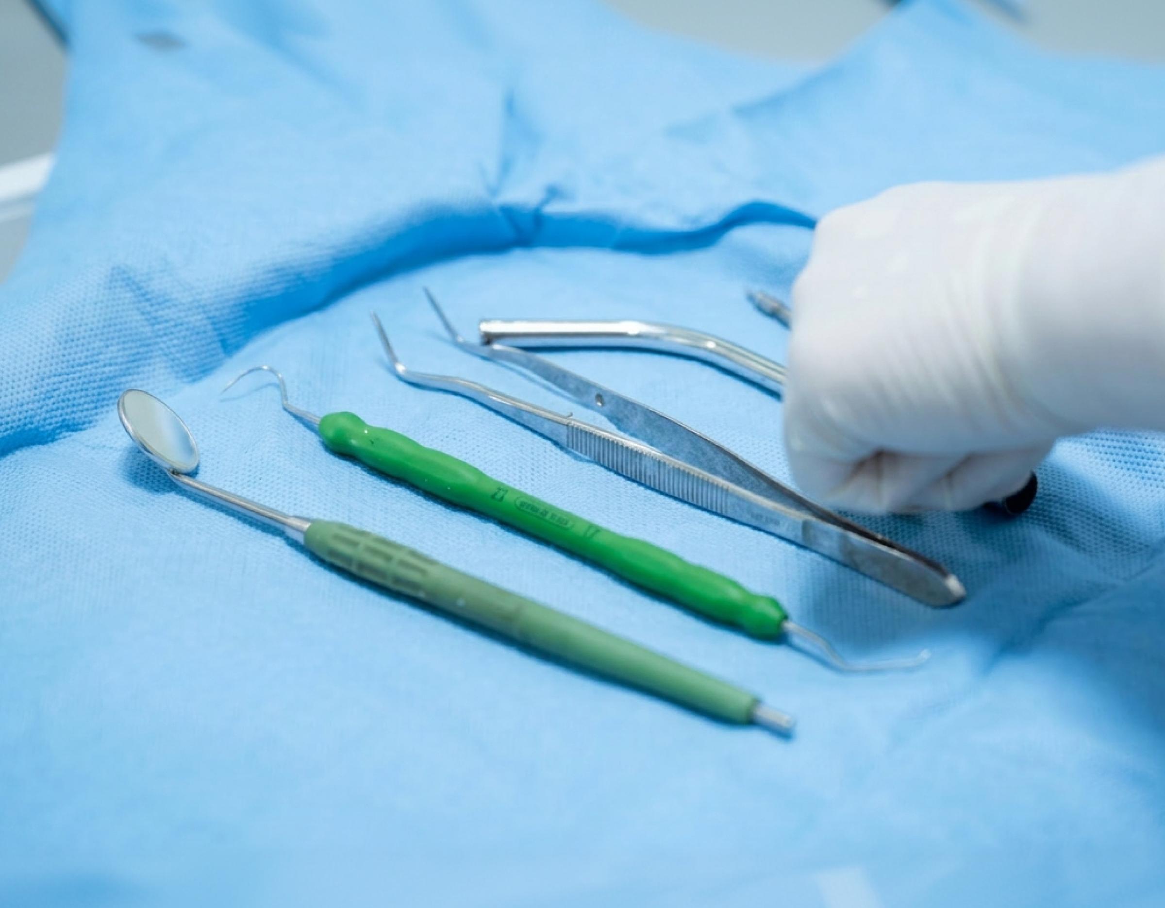 dental instruments—mirror, scaler, tweezer and probes laid on blue surgical drape with gloved hand reaching, 굿윌치과병원 clinic setting