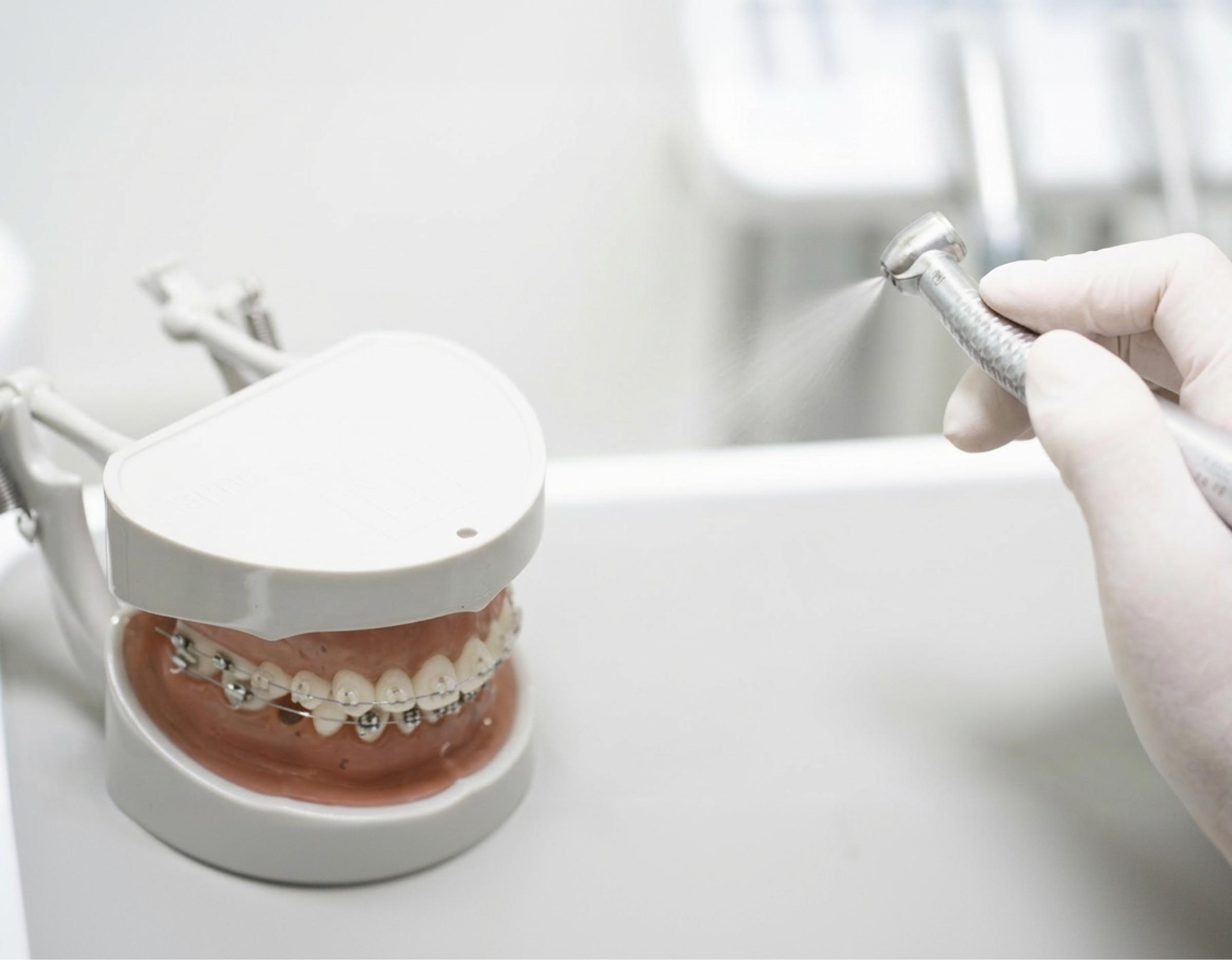 Dental model with metal braces on lower teeth beside gloved hand spraying dental handpiece at 굿윌치과병원 JCI-certified clinic