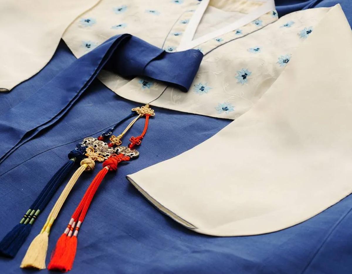 Traditional blue and white hanbok with embroidered collar and colorful norigae tassels for K-뷰티 빛의 공식 tour