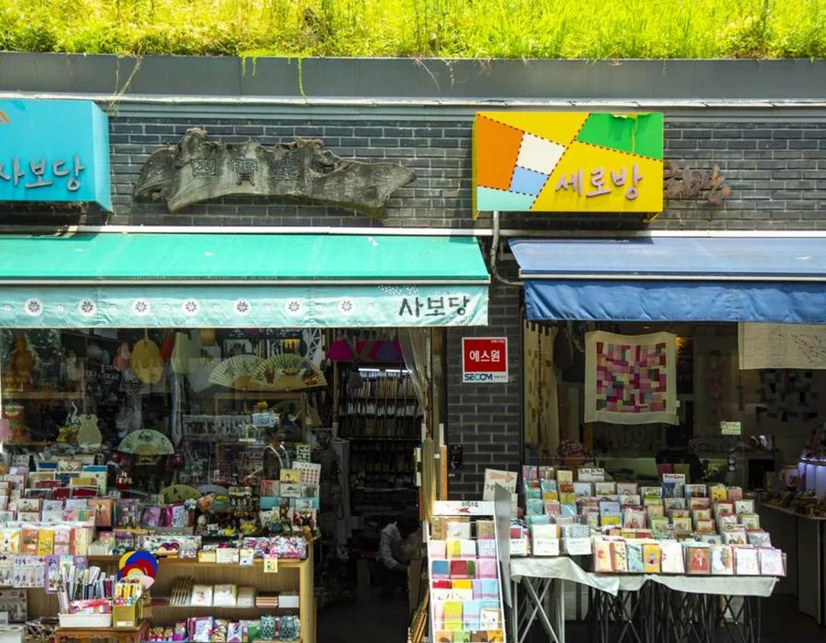 Small Seoul shopfronts with teal and blue awnings displaying colorful stationery, greeting cards and craft supplies on sidewalk tables