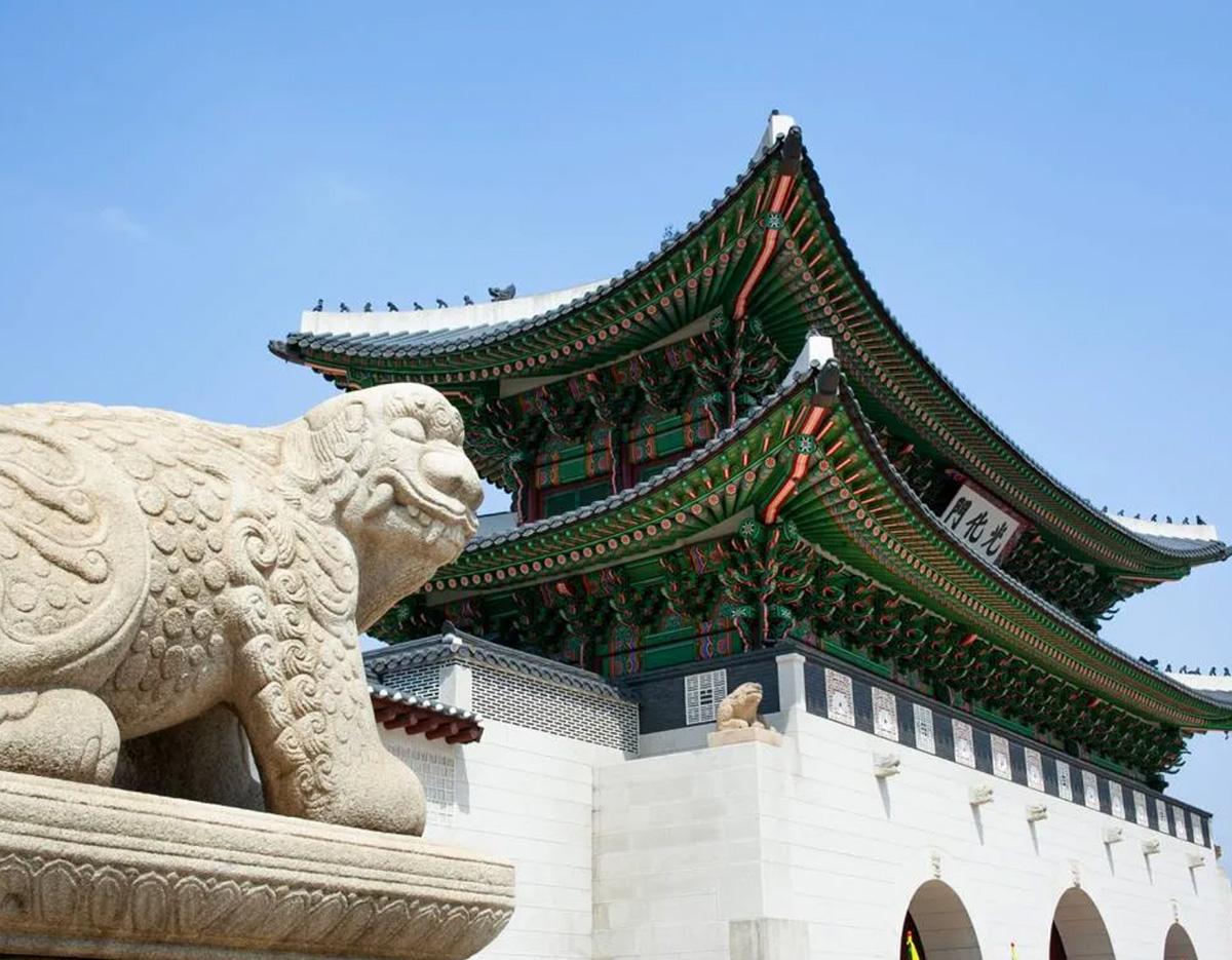 Gyeongbokgung-style palace gate with ornate green and red eaves and a carved stone guardian lion in foreground