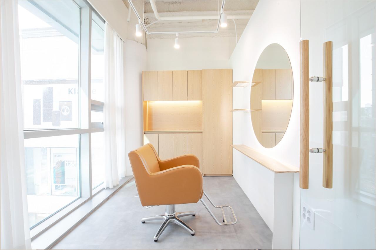 Minimalist salon interior at 로위 홍대입구역점 with tan styling chair, large round mirror, wood cabinets and floor-to-ceiling windows