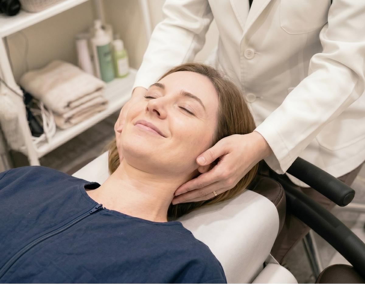 Patient reclining on treatment chair receiving a female practitioner’s hands-on neck adjustment at 케이한의원 | USP clinic.