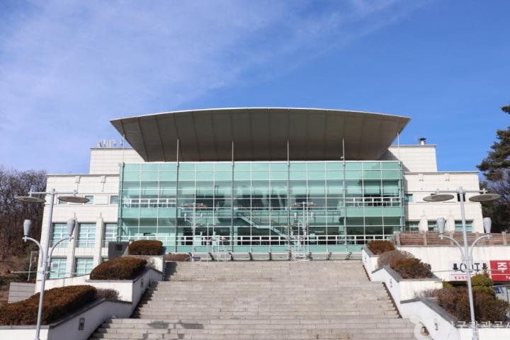 Modern glass-fronted auditorium with wide stone steps leading up to entrance under a large curved roof at 2026 KMCHART AWARDS venue