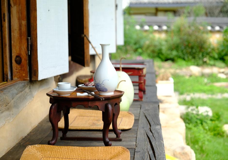 manho gotaek 양동마을 전통주 체험: white ceramic soju bottle and cups on a small wooden table on a hanok wooden porch with cushions and garden beyond