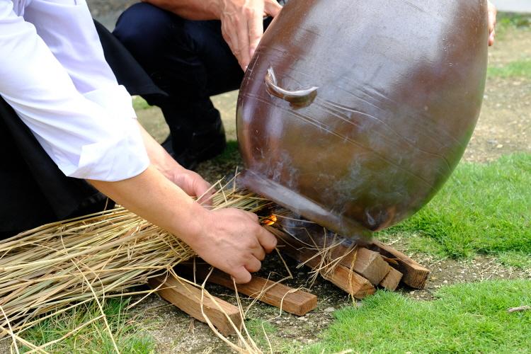 Man lighting straw beneath a large clay sojutgori jar during 만호고택 양동마을 전통주 체험 to heat and sterilize the jar.