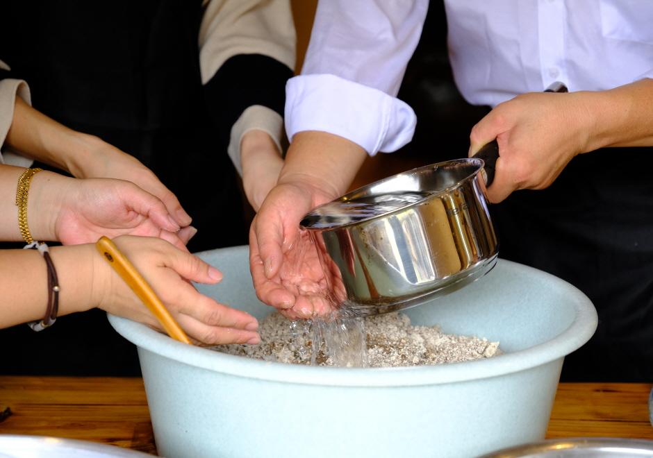 만호고택 양동마을 전통주 체험: hands pouring water from a pot into a basin while stirring grain and nuruk for cheongju brewing