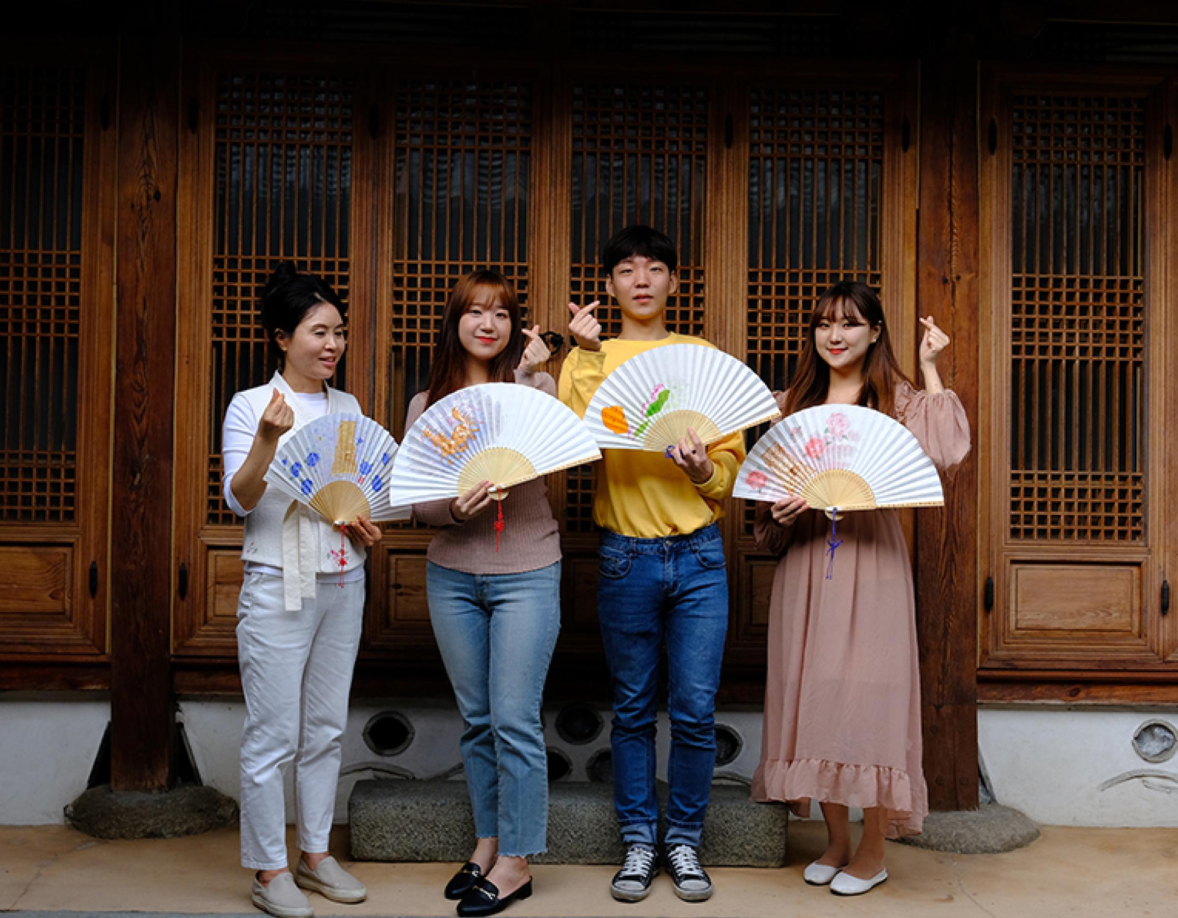 Participants standing in front of a traditional wooden hanok holding hand-painted Silla-era style fans from the Buchae experience in Gyeongju