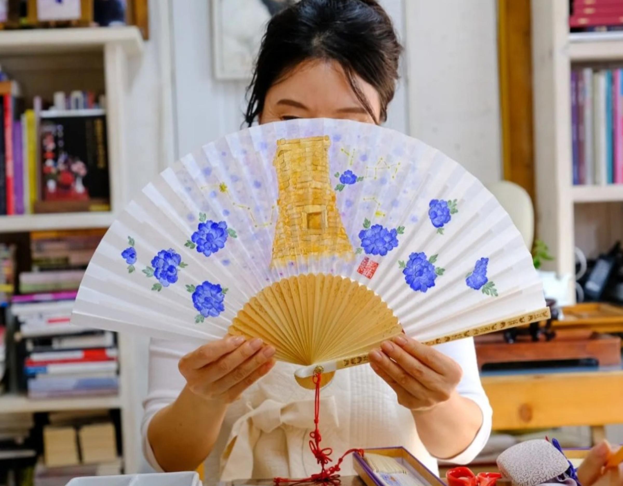 Participant holding a hand-painted folding fan decorated with blue floral Silla-era style motifs during Gyeongju workshop.