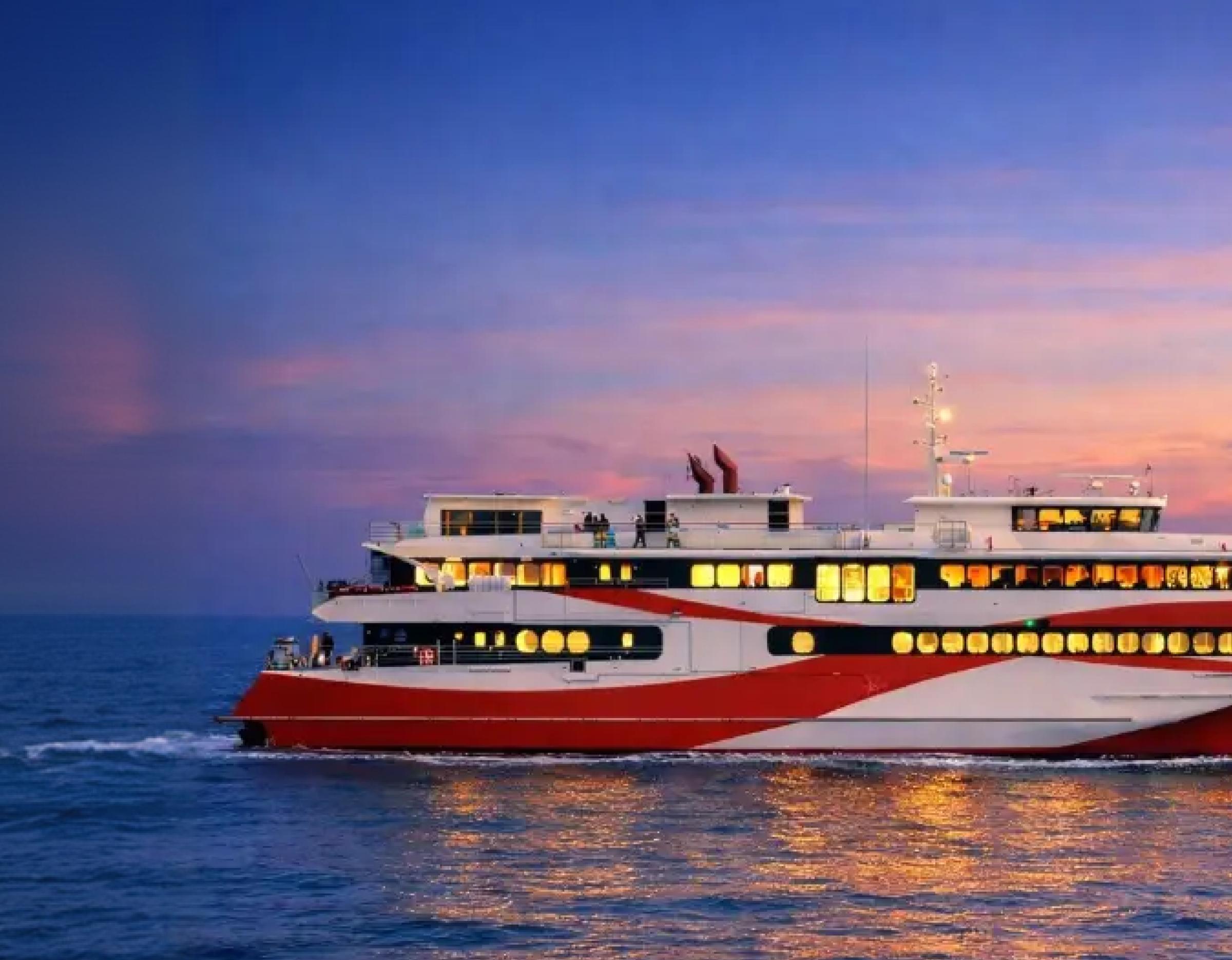 502-seat red-and-white superyacht cruising at sunset with lit windows reflecting on calm sea under colorful sky