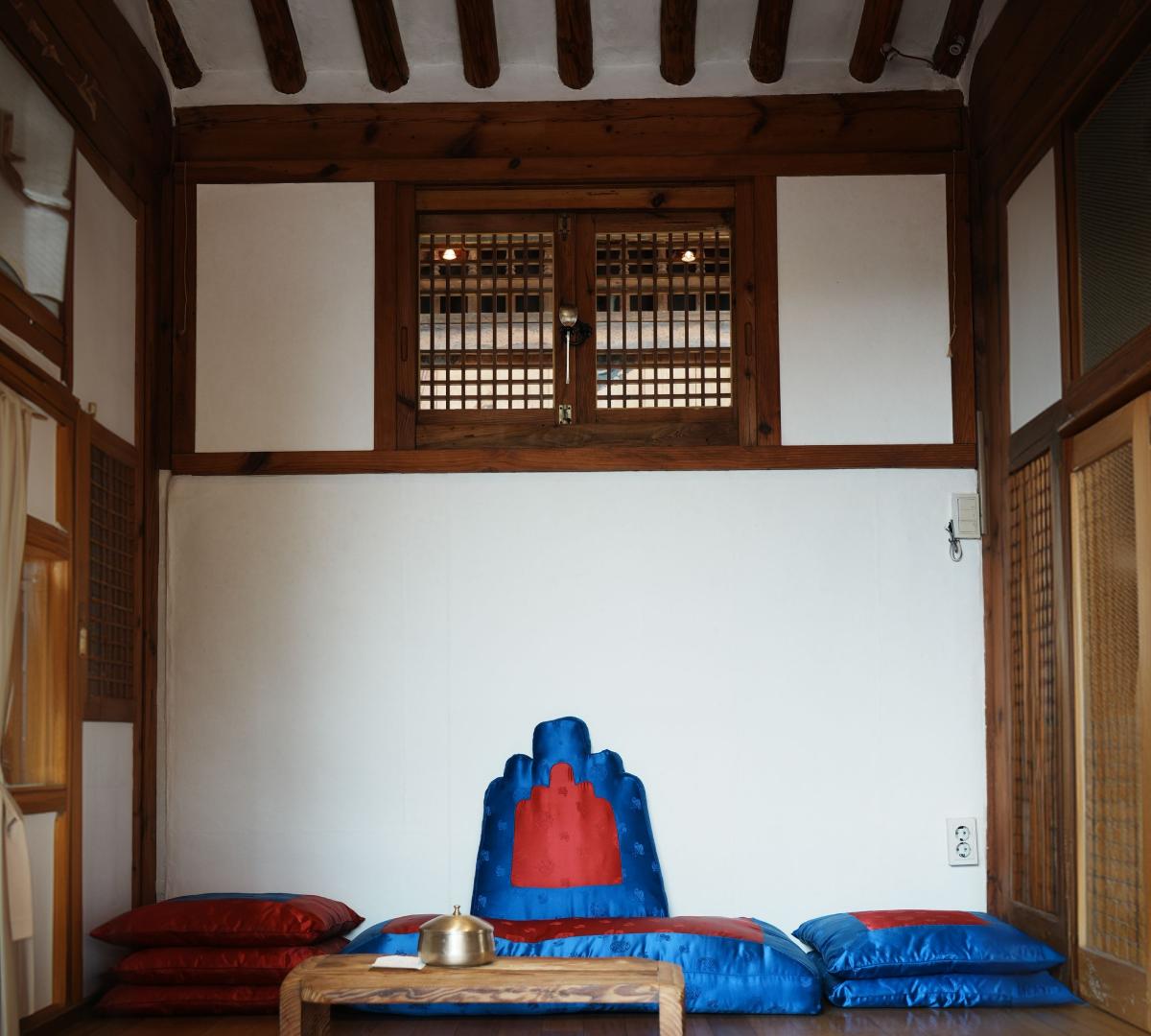 Traditional Korean hanok interior with low wooden table, blue-red silk floor cushions and wooden beams above