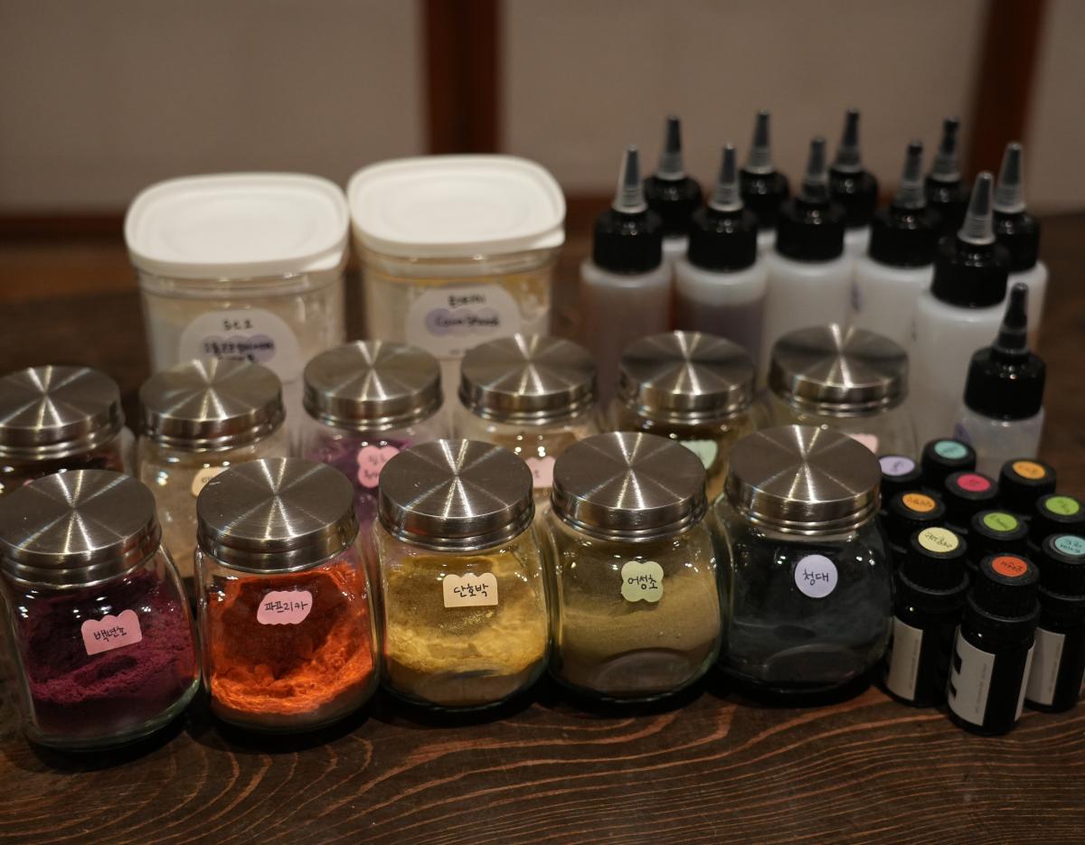 Rows of glass jars filled with colorful natural powder ingredients, squeeze bottles and labeled essential oil vials for shampoo bar class