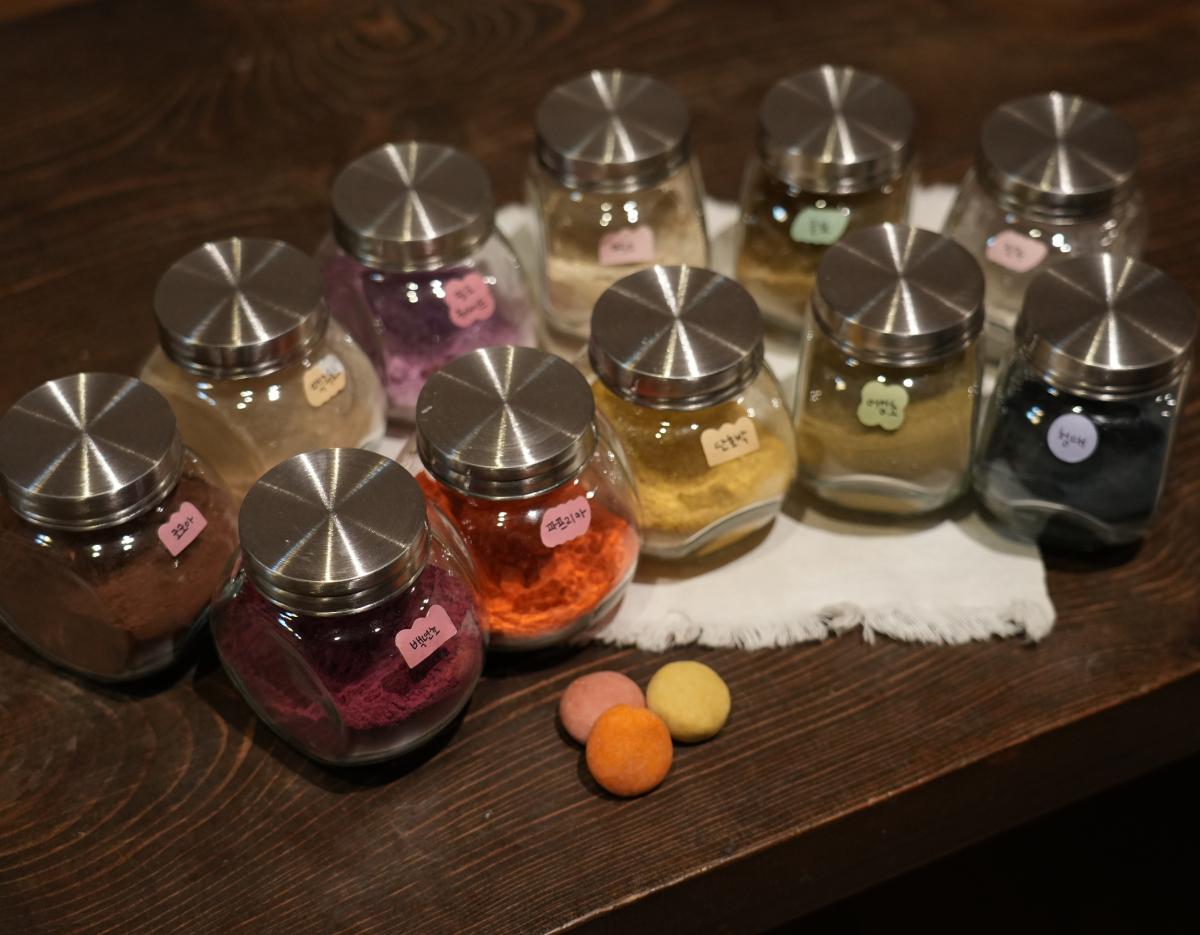 Glass jars of colorful natural powders and three round handmade shampoo bars on a wooden table for 북촌다락방 안국 shampoo bar class