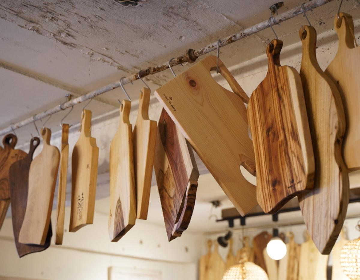 Assorted handcrafted wooden cutting boards with varied shapes and wood grains hanging from a metal rod in a workshop