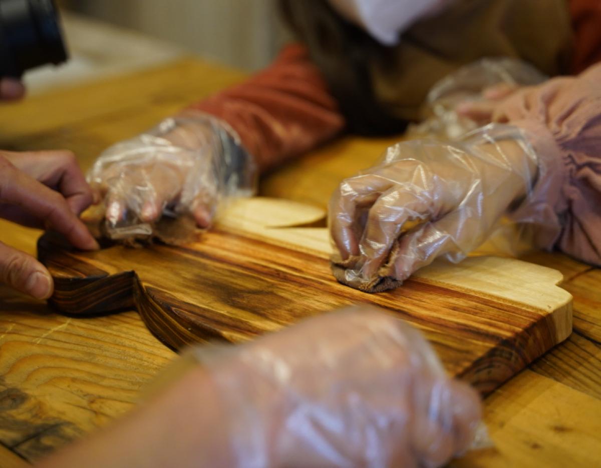 Hands wearing disposable gloves applying finish to a striped wooden cutting board during a 나무 도마 만들기 체험 in Gyeongju