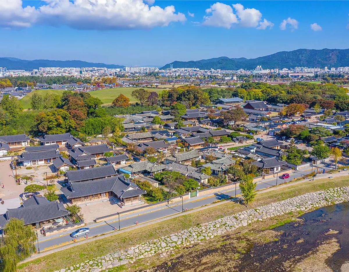Aerial view of Gyochon hanok village in Gyeongju with clustered traditional tiled-roof houses beside a river and distant cityscape