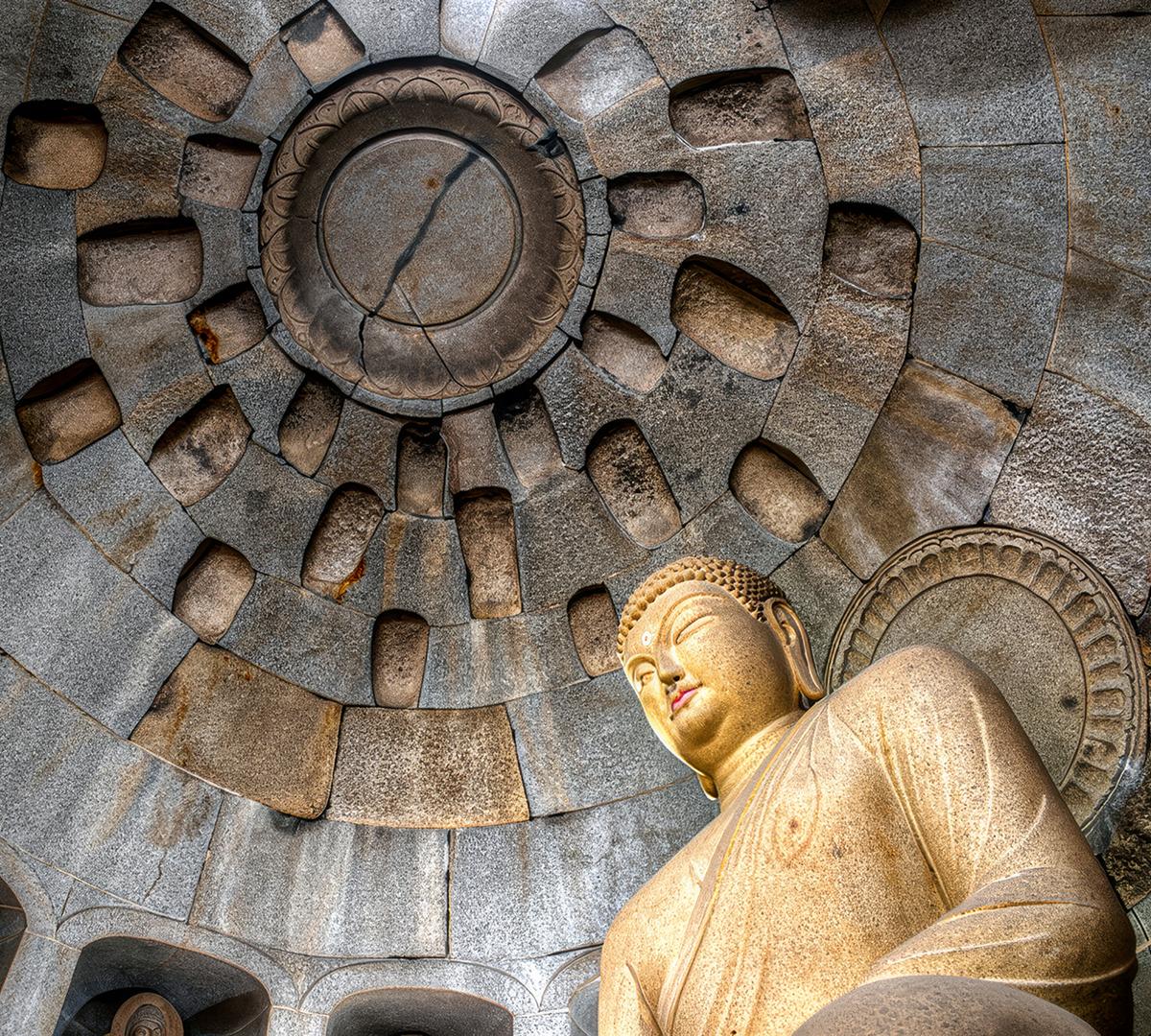 stone Buddha statue seated inside intricately carved circular grotto ceiling at Seokguram grotto in Gyeongju