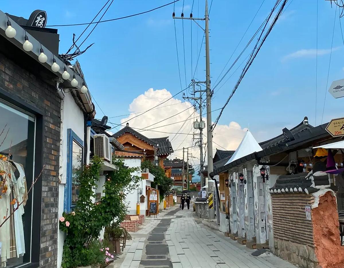 Gyochon Hanok Village narrow stone street lined with traditional hanok buildings, cafes, hanging lights and pedestrians.