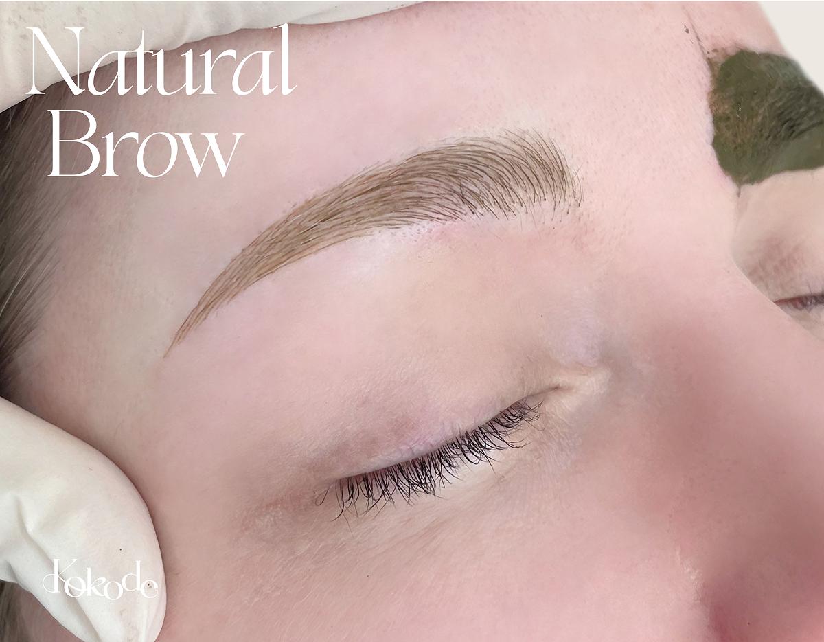 Close-up of a client's closed eye showing a natural-looking microbladed eyebrow with fine hair stroke detail.