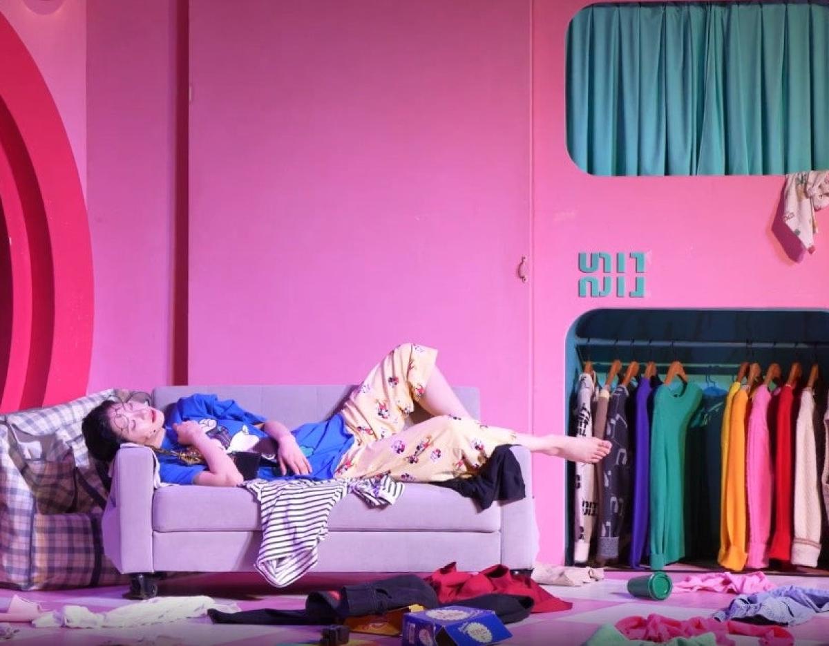 인사이드미 뮤지컬 혜화 scene: actor lounging on a gray sofa amid colorful wardrobe and pink stage set, clothes scattered around