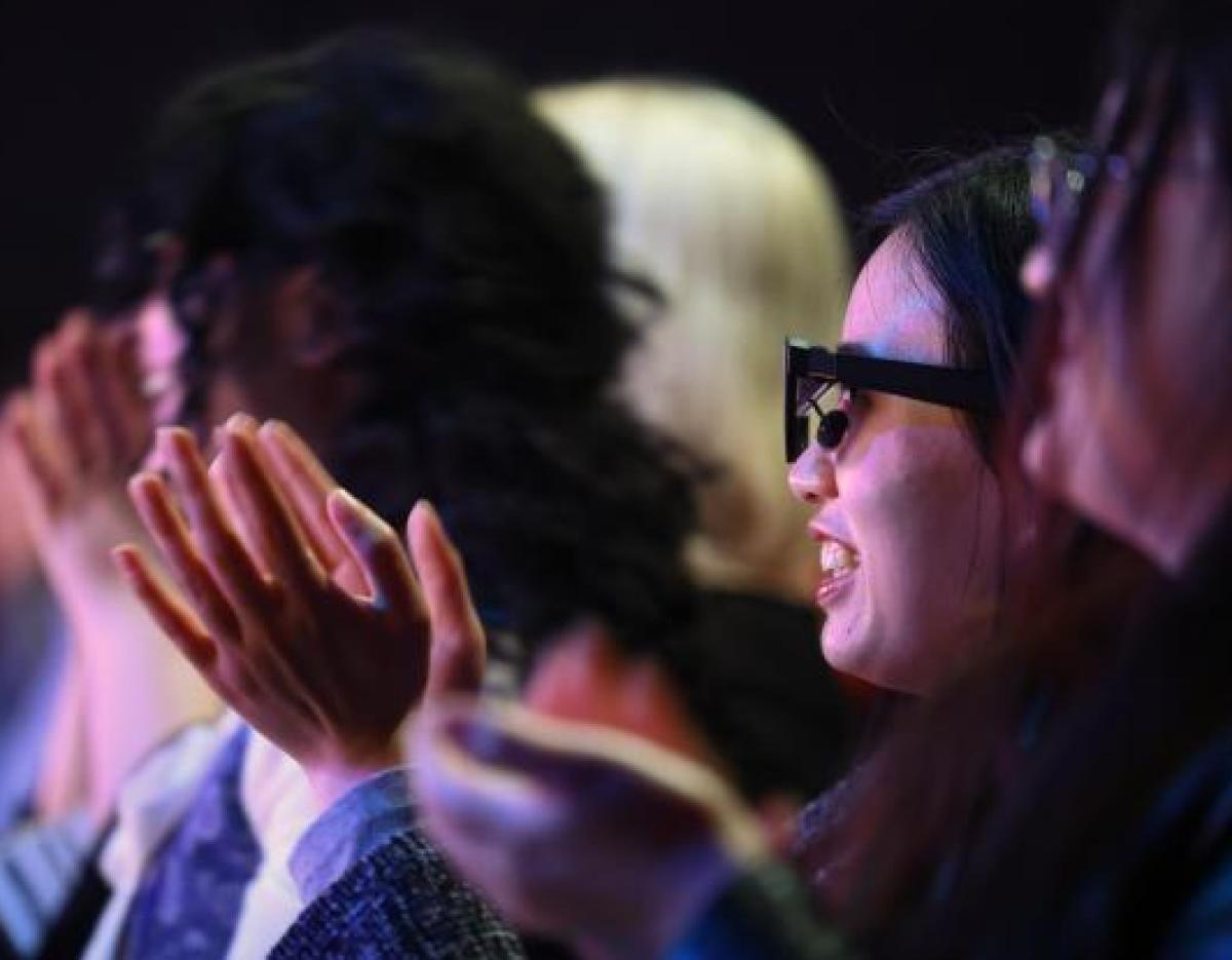 Audience members seated in dark theater clapping hands in applause during a musical performance