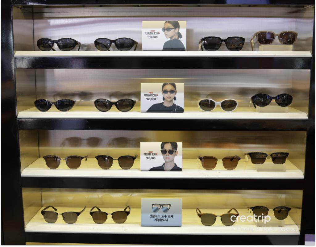 Glass display shelves showing multiple pairs of trendy sunglasses and sample cards with blurred faces and price tags at 룩옵티컬 강남역점.